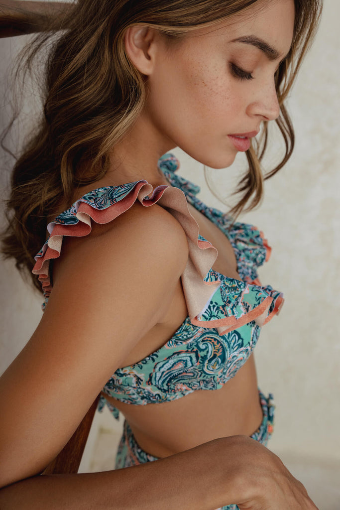 A closer look at side view of the Ruffled Bikini Bra, with double bolero ruffles in contrasting turquoise and orange colors, with contrasting lurex tones on the neckline and straps and over-the-shoulder adjustable straps and ties back, paired with the Reversible High Waist Bikini Bottom. 