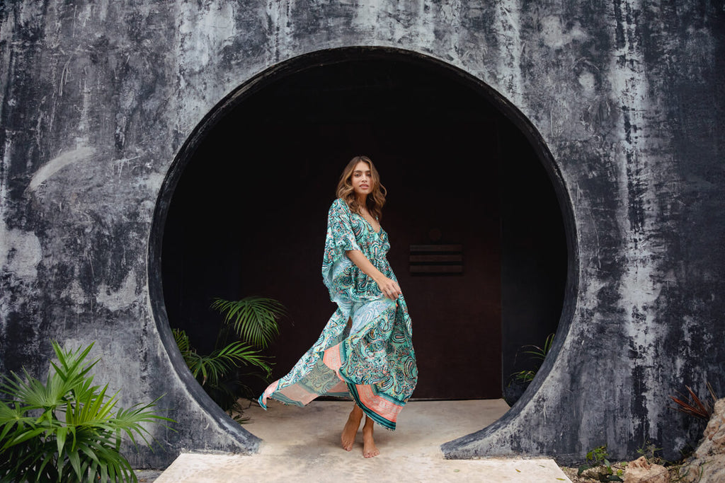 A model casually walking, wearing the Shine Eclectic Vibes Kaftan, a long and elegant kaftan adorned in paisley print, with a gathering on the waist.