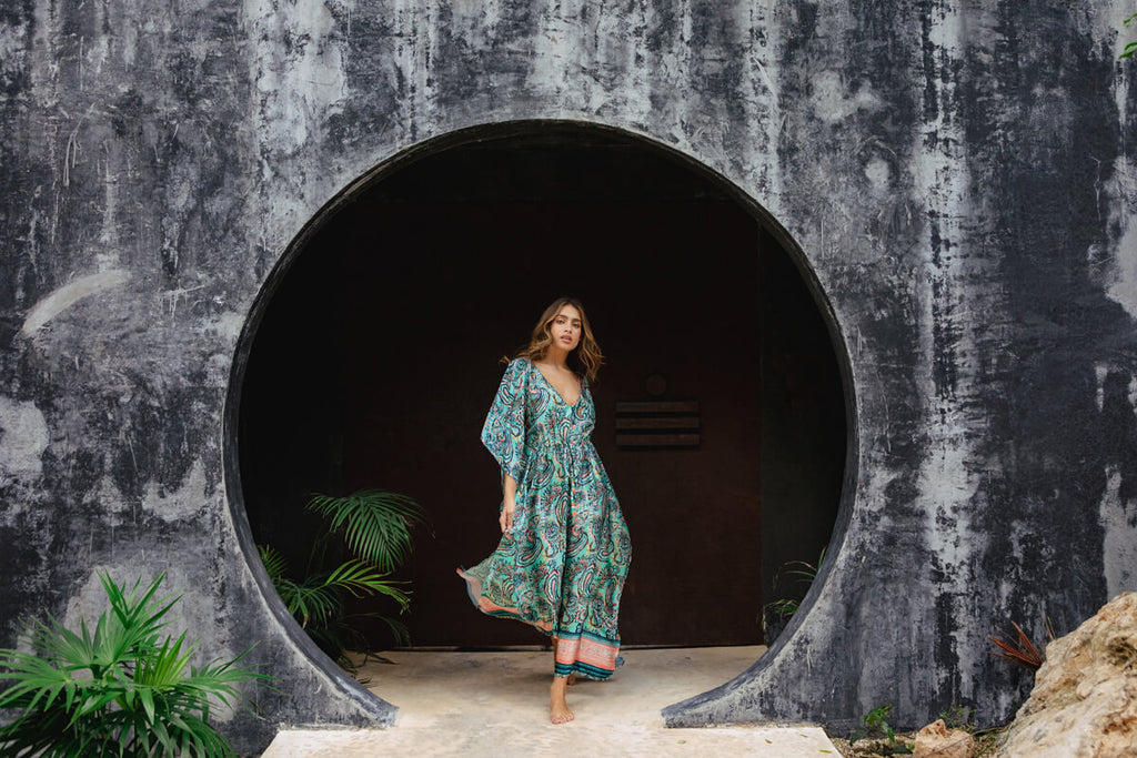 A model casually walking, wearing the Shine Eclectic Vibes Kaftan, a long and elegant kaftan adorned in paisley print, with a gathering on the waist.